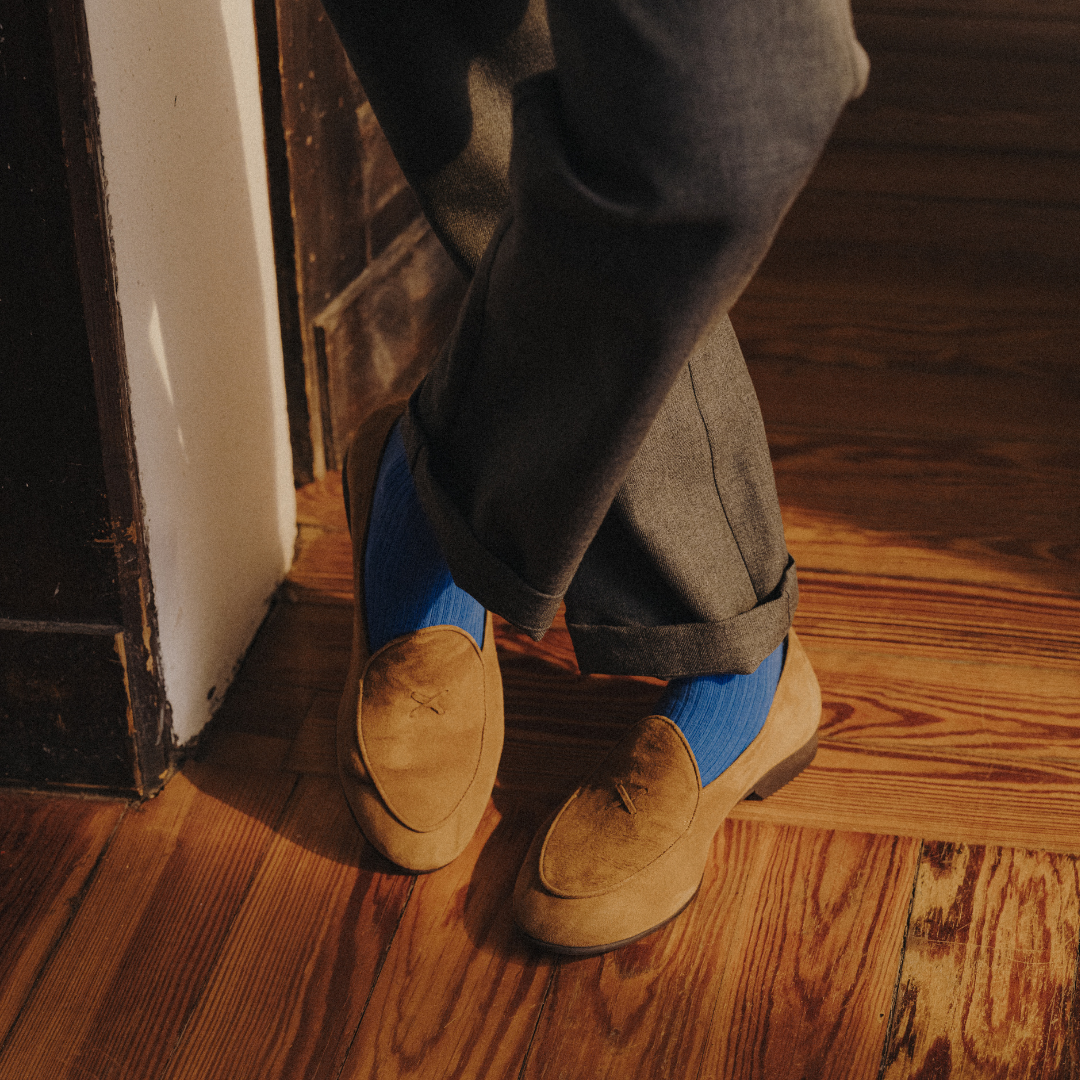 Person wearing brown loafers with blue soles on a wooden floor.
